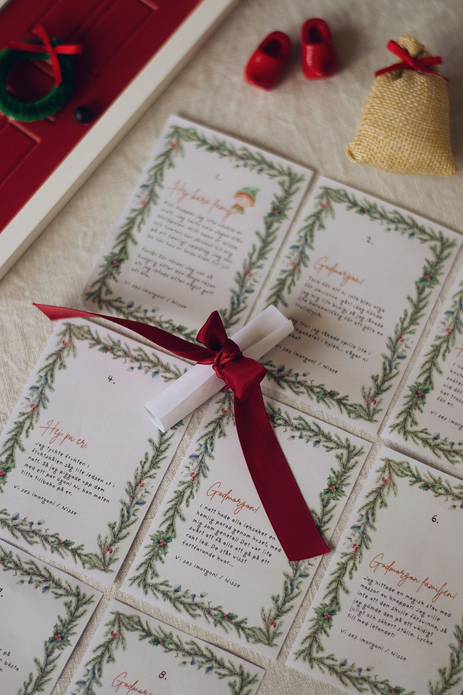 Utklippta nissebrev som du laddar ner och skriver ut för julen 2025. Ett brev är ihoprullat och klätt med en röd julrosett.